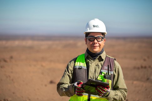 Worker in safety gear with tablet, standing in a desert landscape.